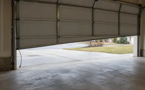 A garage door hanging crooked with a slack lifting cable beside the track
